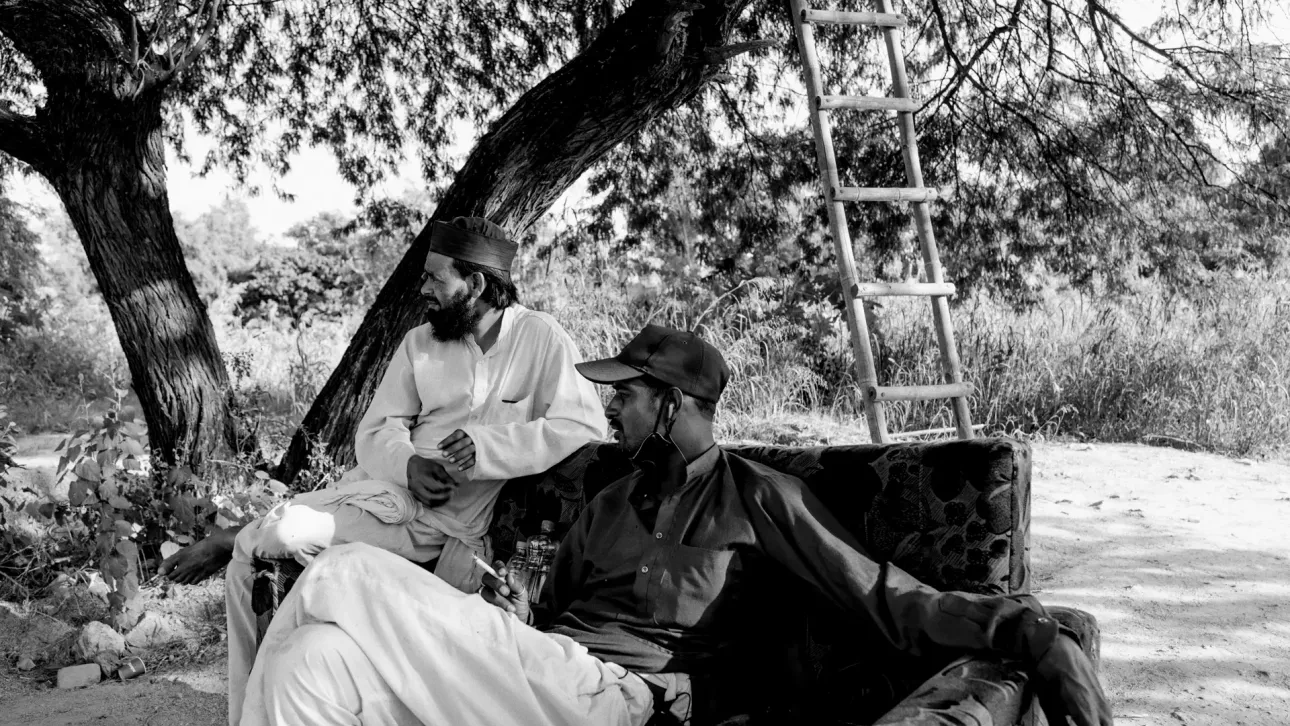 Caretakers at New Delhi’s oldest graveyard, sit on an old discarded sofa at the edge of a Covid-19 burial site