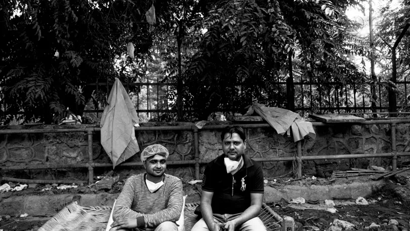 Two Covid-19 ambulance drivers sitting on a straw cot near a cremation ground in New Delhi